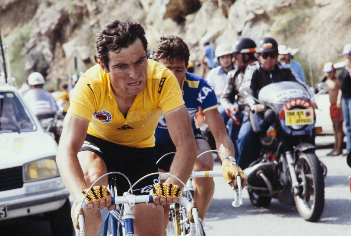 Bernard Hinault celebrating on the Tour de France podium with winner's bouquet and yellow jersey