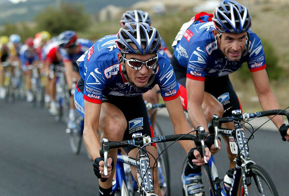 A dense peloton climbing a steep mountain road with team leaders and domestiques pacing the group