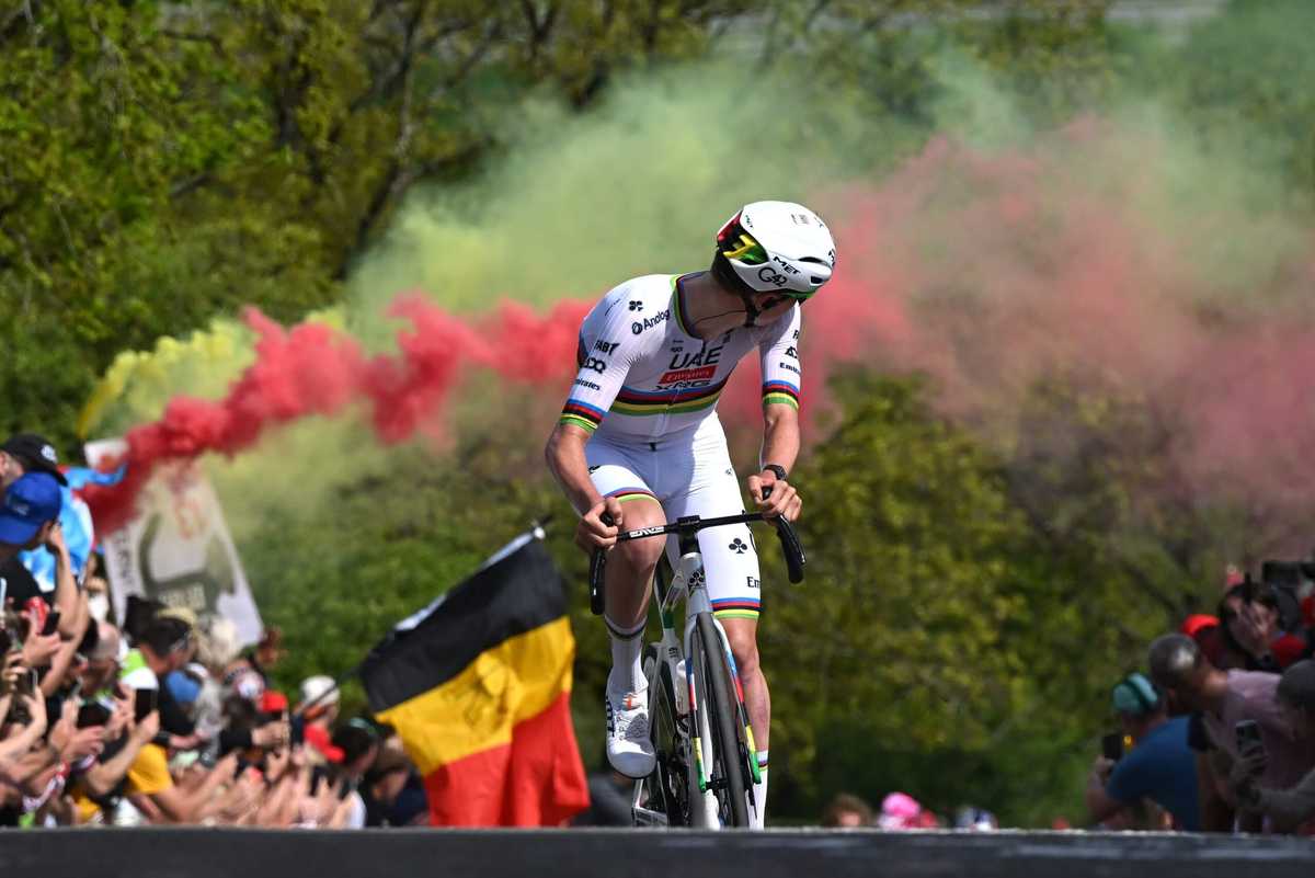 Riders powering over a long cobblestone sector with mud splatter and tense expressions
