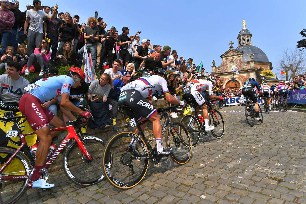 Solo rider powering up a steep cobbled berg with spectators lining the narrow road