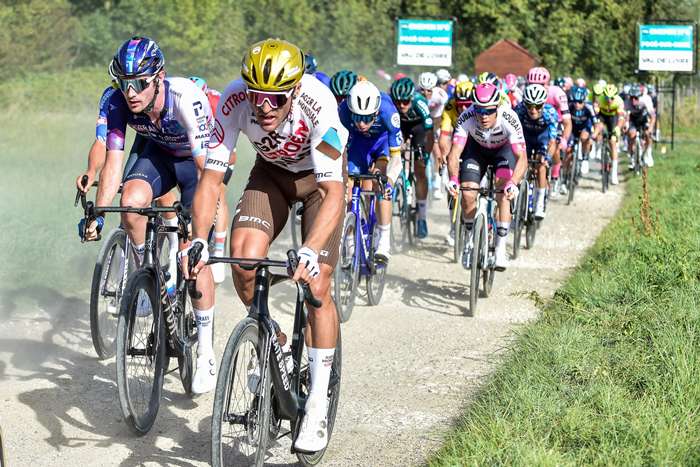Small breakaway group riding across rolling foothills before the main climb while teams watch from behind